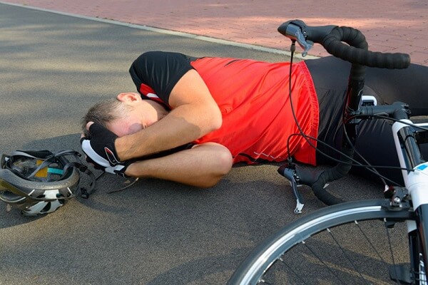 man laying on the ground holding his head after bicycle accident